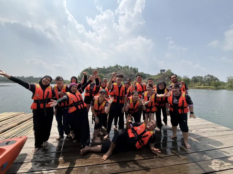 Team smiling together beside a lake after an outdoor challenge
